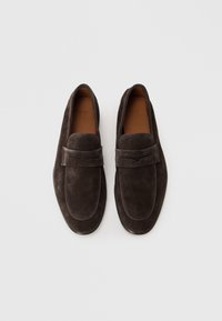 Mocasines de gamuza marrón oscuro con una plantilla de cuero suave y un sutil detalle de costura en el empeine, con una punta redondeada y un perfil bajo.
