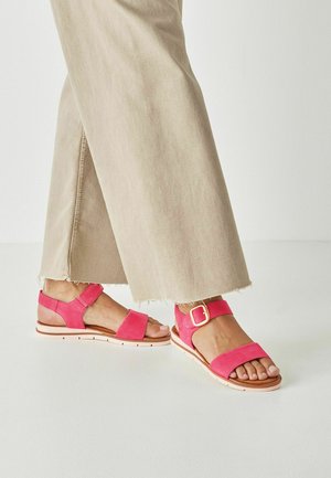 Roze suède sandalen met twee bandjes, waarvan één met gesp, en een gevoerde zool. Gecombineerd met lichtbeige broek met rafelige zoom.