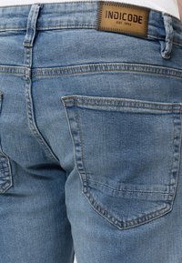 Lyseblå denim jeans med baglommer og en brun læderlabel med "INDICODE EST. 1993" syet på linningen.