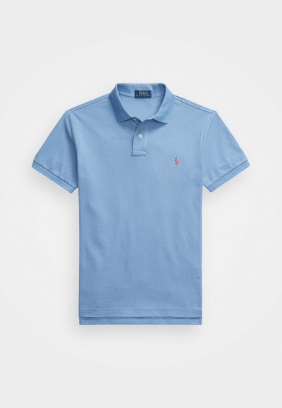 Gaiši zils kokvilnas polo krekls. Tam ir klasiskas formas apkakle, īsas piedurknes un mazs izšuvums kreisajā krūtīs.