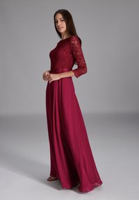 Burgundy aftonklänning med en åtsittande spetsöverdel och trekvartslånga ärmar, flödande A-linjeformad kjol och en subtil lyster i tyget.