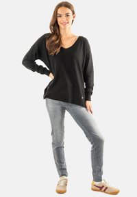 Suéter negro de gran tamaño con escote en V, corte relajado, combinado con jeans de color azul claro y zapatillas beige con acentos de color.
