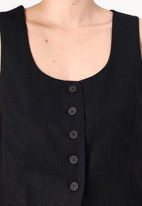 Vestido de linho preto com acabamento em decote redondo e seis botões na frente. O tecido tem uma aparência texturizada e um brilho mínimo.