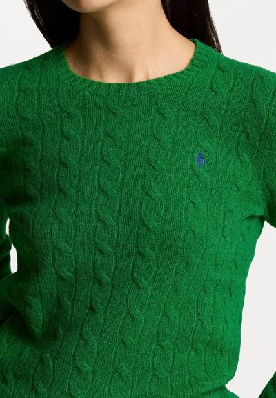 Pull vert en tricot torsadé fait de tissu doux, avec un col rond et un petit logo bleu sur la poitrine. Texture riche et détails de motif.