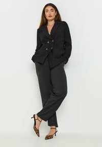 Svart dubbelknäppt kavaj med guldknappar, matchande byxor. Skorna har leopardmönster med ankelremmar.