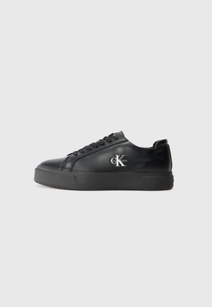 Black leather sneaker with a rounded toe, flat black sole, and tonal lacing. Features a silver logo on the side, smooth texture throughout.