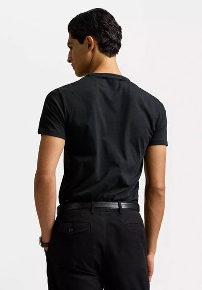 Maglietta nera aderente a maniche corte, realizzata in cotone. Il retro presenta un collo a giro e una texture liscia, abbinata a pantaloni neri.