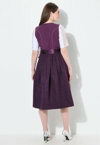 Paarse jurk met een gestructureerd bloemmotief, een satijnen ceintuur in de taille en kanten mouwen. De jurk heeft een uitlopende rok en plooien. Zilverkleurige hakken.