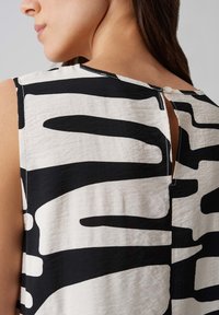 Top senza maniche realizzato in tessuto leggero con un motivo astratto in bianco e nero. Chiusura posteriore con un piccolo bottone e dettaglio a spacco.