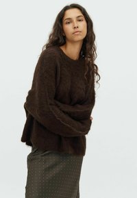 Brown, fluffy knit sweater with a round neckline, long sleeves, and a relaxed fit. Paired with a dark green polka dot skirt.