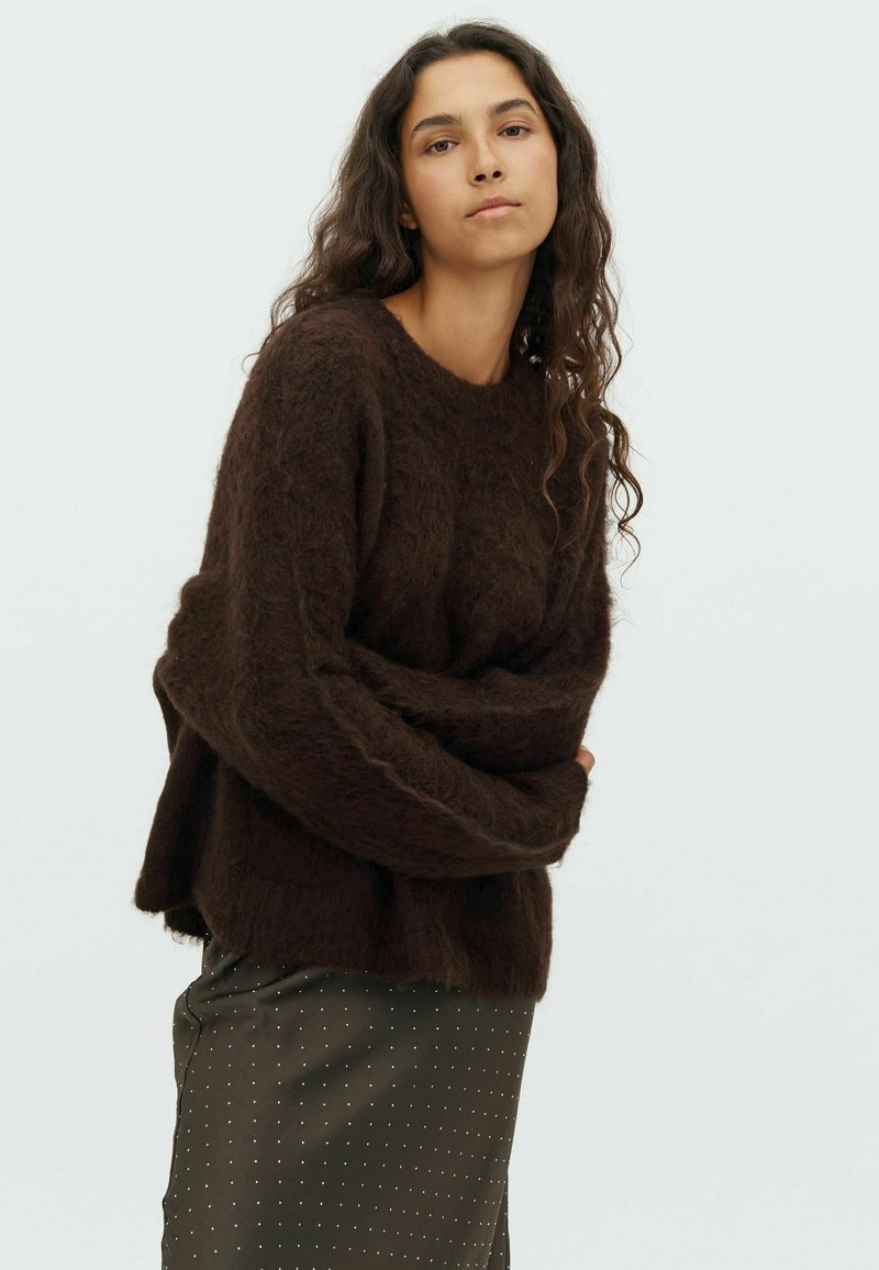 Brown, fluffy knit sweater with a round neckline, long sleeves, and a relaxed fit. Paired with a dark green polka dot skirt.