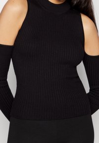 Czarny prążkowany top dzianinowy z wysokim dekoltem i wycięciami na ramionach. Długie rękawy sięgają nadgarstków, tworząc dopasowaną sylwetkę.
