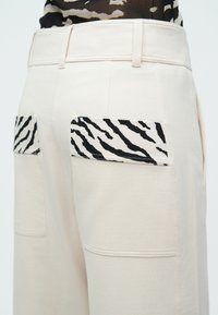 Φαρδιά μπεζ παντελόνια με τσέπες-μπαλώματα σε μαύρο και άσπρο σχέδιο ζέβρας. Ομαλή υφή με ραφές προσαρμοσμένης ραπτικής.