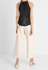 Black sleeveless lace top with a halter neck, paired with cream wide-leg pants featuring frayed hems and block-heeled sandals.