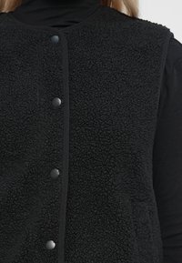 Zwarte fleece vest met een gestructureerde stof, ronde halslijn en drukknoopsluiting; inclusief steekzakken en contrasterende bies.