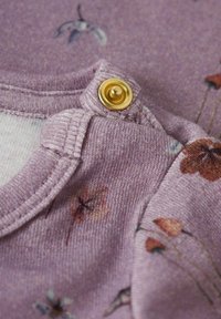 Gros plan sur un vêtement pour bébé floral violet montrant un bouton-pression doré et un col côtelé avec des motifs de fleurs délicats.