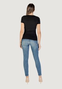 T-shirt nero a maniche corte abbinato a jeans fitted di un blu chiaro, con un design semplice e una texture liscia, indossato con tacchi alti nude.