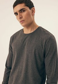 Langarmiger grauer Shirt aus weichem Stoff, mit Rundhalsausschnitt und minimalen Nahtdetails an der Schulter.