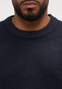 Mörkblå stickad tröja med ribbad rundhalsning och texturmönster, med en kroppsnära passform och mjukt tyg.