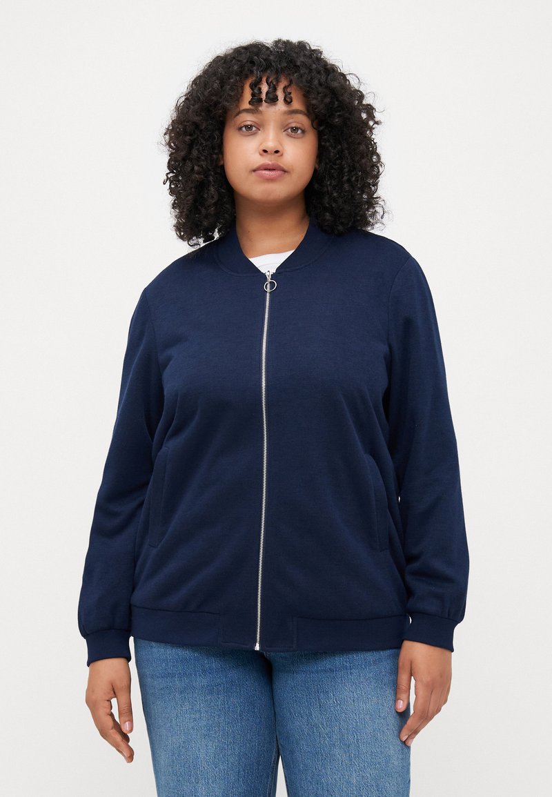 Navy zip-up bomber jacket with ribbed cuffs and hem, featuring a round neckline and two side pockets. Soft, textured fabric.