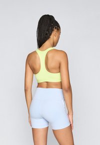 Αθλητικό σουτιέν σε νεον πράσινο χρώμα με σχέδιο racerback, συνδυασμένο με μπλε σορτς ψηλής μέσης, κατασκευασμένα από ελαστικό ύφασμα με λεία υφή.