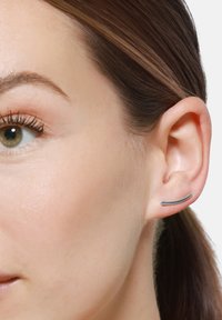 Orecchino in metallo argento con un design elegante e curvo. Esposto sull'orecchio di un modello, evidenziando il suo stile minimalista e moderno.