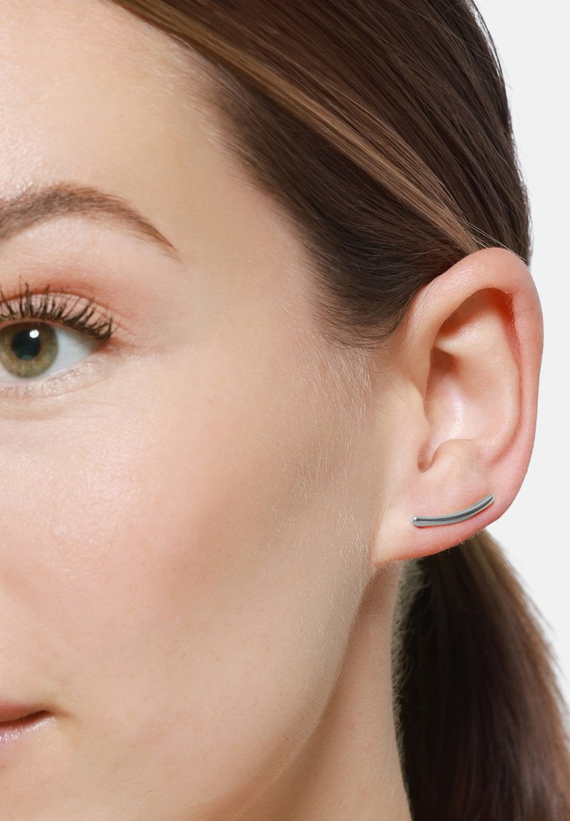 Orecchino in metallo argento con un design elegante e curvo. Esposto sull'orecchio di un modello, evidenziando il suo stile minimalista e moderno.