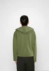 Sudadera con capucha verde de corte relajado, fabricada en un material suave. Presenta un dobladillo curvado y hombros caídos para un look casual.