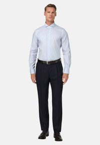 Světle modrá, pruhovaná košile s rozhaleným límcem, kombinovaná s přizpůsobenými námořnickými kalhotami a černým opaskem, na bílém pozadí.