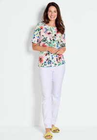 Blumen-T-Shirt mit kurzen Ärmeln in Pink-, Grün- und Blautönen; kombiniert mit weißen Hosen und gelben Sandalen. Weicher Stoff mit lässiger Passform.