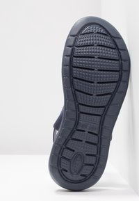 Semelle d’une sandale bleu foncé avec une bande de roulement texturée et des rainures, affichant le nom de la marque "crocs" sur la zone du talon.
