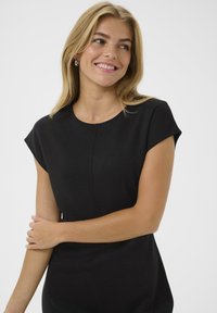 Melnas īsām piedurknēm kleitas ar apaļu kakla izgriezumu, kas ietver smalku šuvi priekšpusē un gludu, pieguļošu siluetu.