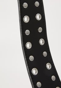 Svart läderbälte med silvermetallspikar och öglor längs hela längden, med synlig sömnad längs kanterna.