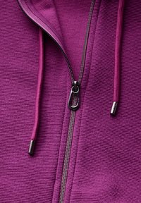Giacca viola con zip realizzata in un tessuto testurizzato. Presenta una zip a contrasto e lacci in una tonalità di viola più scura.