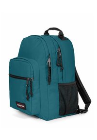 Tyrkysový batoh s několika přihrádkami, včetně přední kapsy na zip a boční síťované kapsy, vyrobený z odolné látky. Černé popruhy a doplňky.