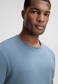 T-shirt bleu clair à col rond en tissu doux, doté de manches courtes et d'une texture lisse, avec des coutures minimales au niveau de l'encolure.