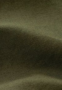 Gros plan sur un tissu vert olive texturé avec un motif tissé visible et de doux plis créant des ombres douces.
