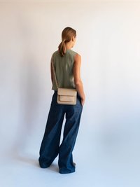 Béžová crossbody taška, hladká textúra, obdĺžnikový tvar. Olivovo zelený top bez rukávov, jemná tkanina. Široké tmavé džínsy, voľný strih.