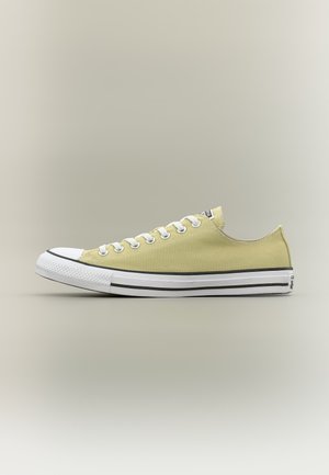 Zapatilla baja de lona amarilla con puntera de goma blanca, cordones blancos y suela blanca con raya negra, vista lateral.