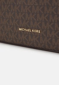 Brun Michael Kors håndtaske med et mønstret stof med sammenkoblede "MK" logoer og et guld brandnavn som accent. Tekstureret overflade, rektangulær form.