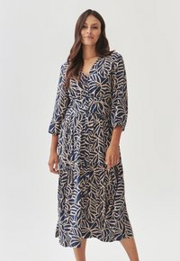 Vestido estampado en azul marino y beige, con un patrón de hojas, escote en V, mangas de tres cuartos y una silueta larga y acampanada con detalle de botones.