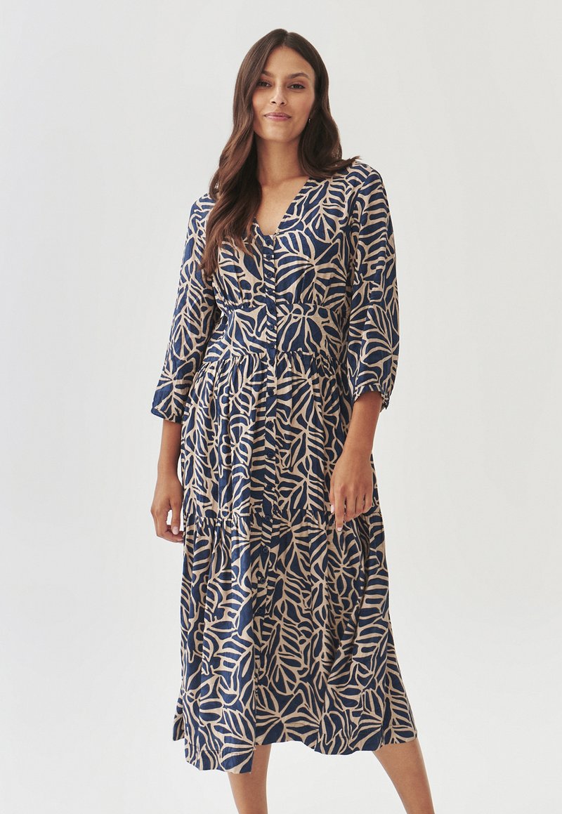 Vestido estampado en azul marino y beige, con un patrón de hojas, escote en V, mangas de tres cuartos y una silueta larga y acampanada con detalle de botones.