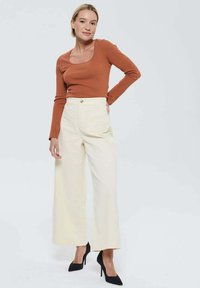 Haut ajusté de couleur rouge rouillé à manches longues avec un col rond, associé à un pantalon large crème taille haute et des escarpins noirs à bout pointu.