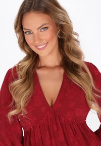 Vestido rojo con escote en V profundo y bordado floral. Tejido suave y texturizado con mangas largas y plisado en la cintura.