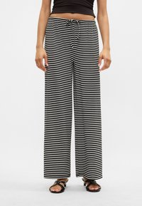 Calças largas às riscas preto e branco com cintura elástica e cordão, apresentando um tecido suave e um corte descontraído.