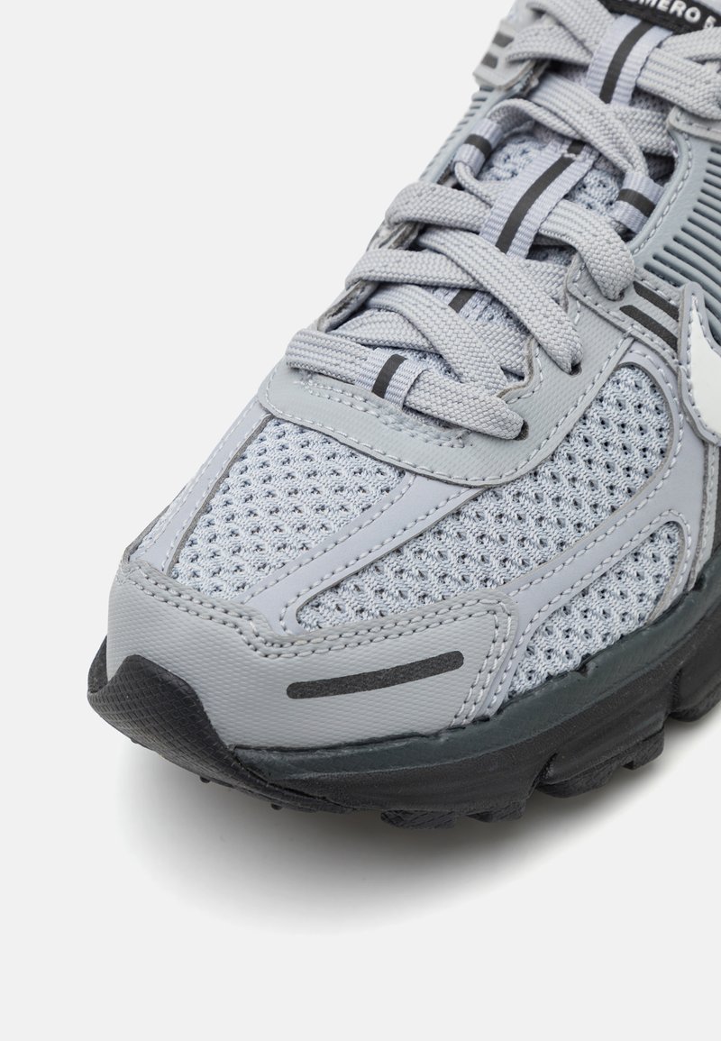 Grauer Sportschuh aus Netz- und Synthetikmaterialien, mit strukturierten Oberflächen, kontrastierenden schwarzen Akzenten und verstärkter Zehenkappe.