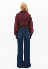 Burgundy genomskinlig skjorta med knappar och lång ärm, ihop med högmidjade, vida blå denimjeans med en brun läderetikett på baksidan.