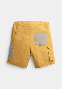 Shorts jaunes en tissu doux, avec une taille élastique, deux poches arrière et une poche latérale avec un panneau en accent gris.
