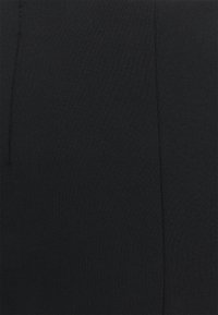 Černé legíny vyrobené z elastické tkaniny, s hladkým povrchem a elastickým pasem pro pohodlí. Po stranách probíhá šev.