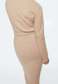 Abito a maglia beige con maniche lunghe, silhouette aderente, dettagli a costine in vita e sulle maniche, texture morbida con una finitura liscia.